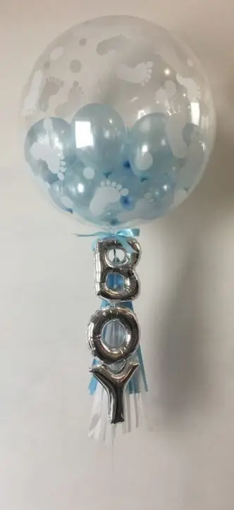 A large clear round balloon with silver "It's a boy" lettering and a matching tassel, created by Balloons Lane in Brooklyn. The balloon is a festive and playful decoration, perfect for celebrating the arrival of a baby boy.