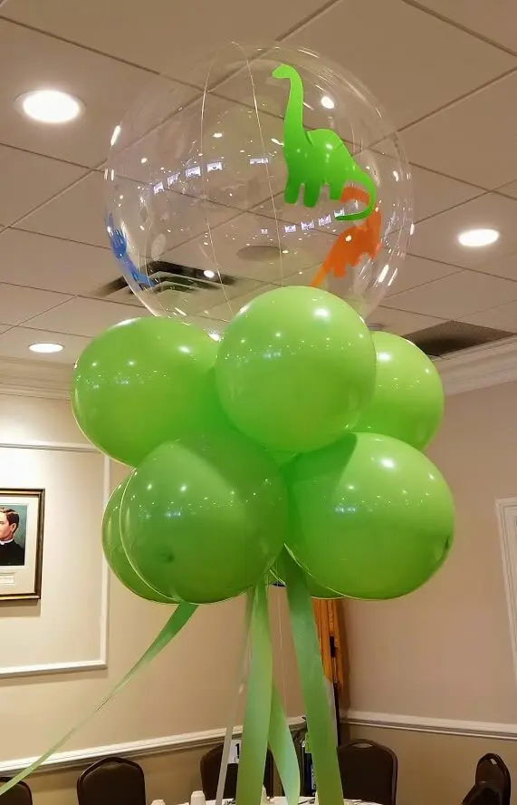 Jumbo-sized clear round balloon with dinosaur theme 1st birthday decorations, including green, mylar balloon centerpiece, by Balloons Lane in Staten Island.