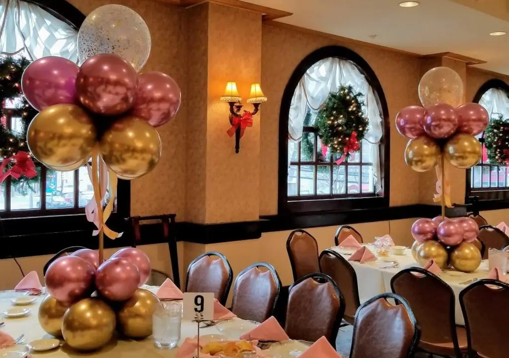 A playful and festive decoration for a baby shower, featuring pink and gold latex balloons and gold confetti balloons arranged in a decorative manner. The centerpiece creates a fun and celebratory atmosphere for the event.