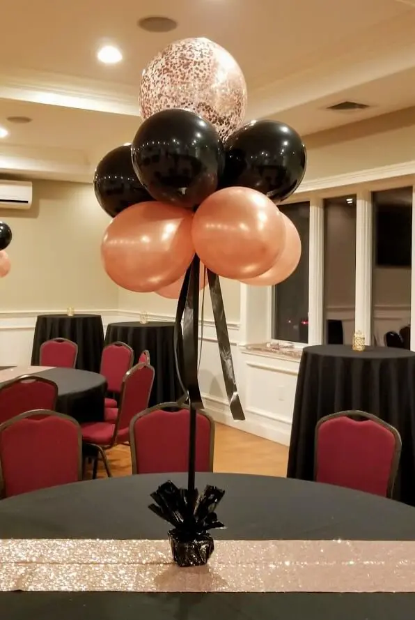 A stylish and elegant centerpiece for an anniversary party, featuring rose gold and black balloons arranged in a decorative manner. The balloons create a festive and romantic atmosphere for the celebration.