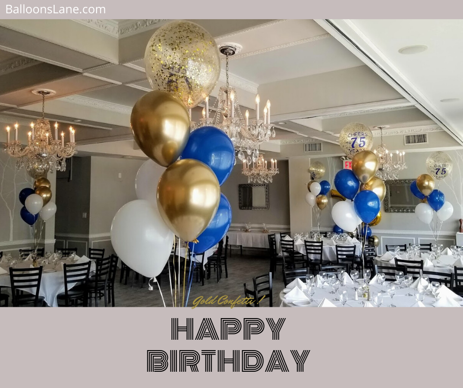 A festive balloon centerpiece featuring blue, gold, and white confetti balloons arranged down the center of a table on Balloons Lane in Staten Island. The balloons are tied to a weight and appear to be floating in the air, adding a fun and celebratory touch to a birthday party.