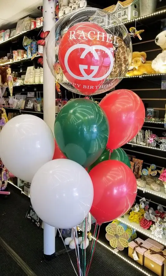 A vibrant Italian-themed balloon centerpiece created for a birthday party on Balloons Lane. The centerpiece features large red, green, and white balloons arranged in a festive column and tied to a weight at the base. Smaller balloons in the same colors are also scattered around the base of the centerpiece, adding to the celebratory atmosphere.