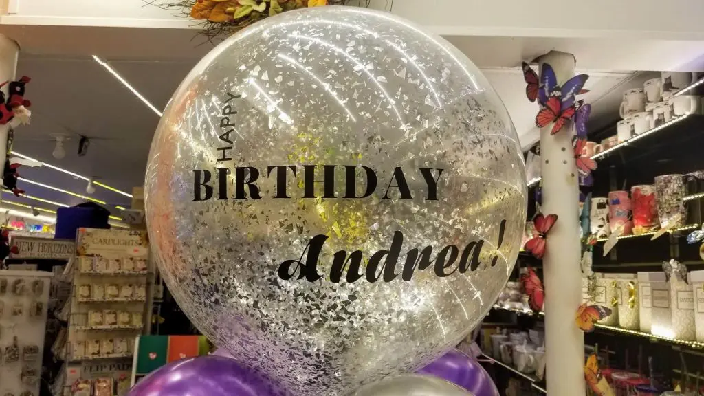 A collection of silver latex balloons, colorful confetti-filled balloons, and a round silver confetti balloon with a personalized "Happy Birthday" message and name.