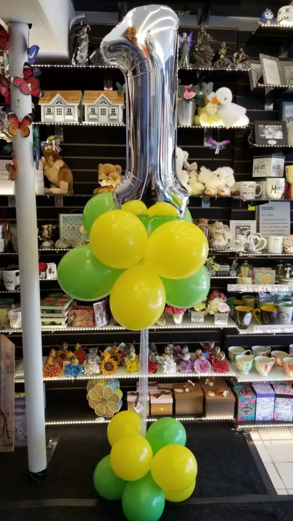 A bouquet of balloons featuring yellow, green, and silver colors, along with number balloons in silver, arranged in NYC.