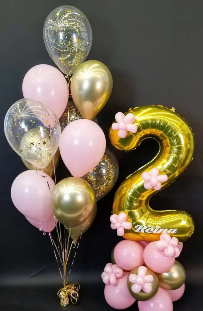 A beautiful balloon column in pink, gold, and chrome gold colors, featuring gold number balloons 2, and filled with pink, gold, and clear confetti, created by Balloons Lane in NYC for a 2nd birthday celebration.