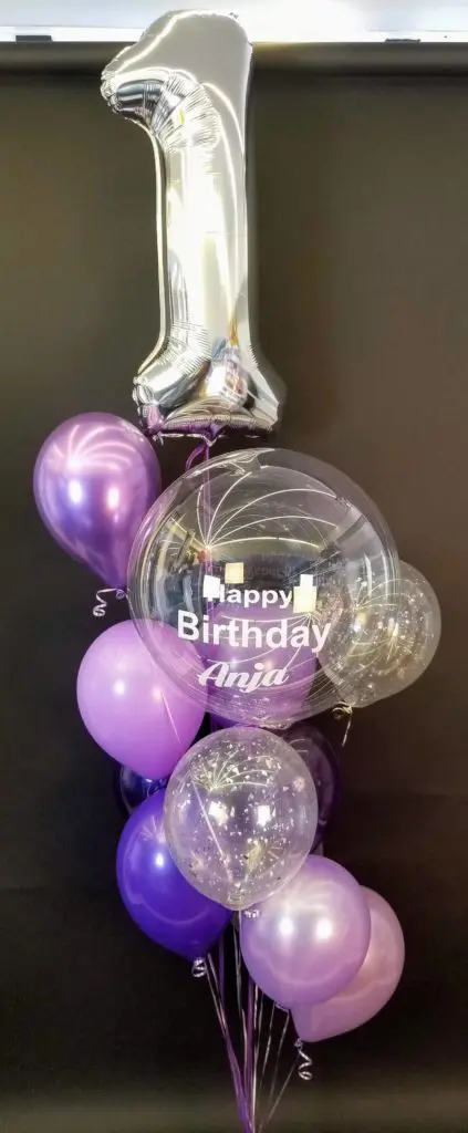 An elegant centerpiece with lavender purple and silver balloons, with large silver number 1 balloon as the highlight.
