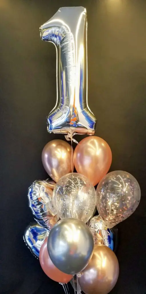 A stunning balloon column in silver and rose gold colors, featuring heart-shaped balloons in silver and magenta number 1 balloons, created by Balloons Lane in NYC for a baby boy's first birthday celebration.
