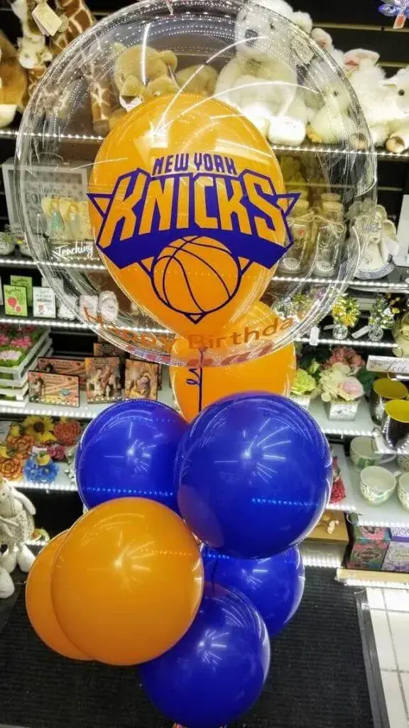 A clear, large balloon filled with a customized sports orange balloon, surrounded by blue and orange balloons, perfect for a sports-themed event.